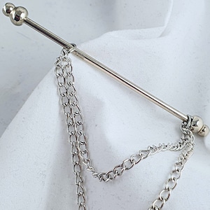 Op de afbeelding: Een zilveren stropdasgesp met aan elk uiteinde een ketting. De ketting is gemaakt van kleine, met elkaar verbonden cirkels.
