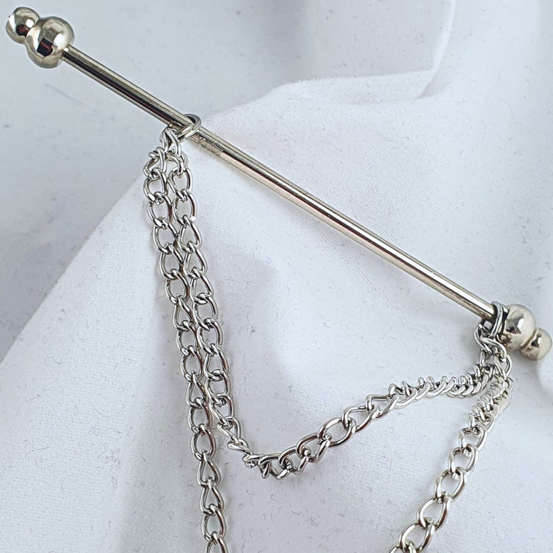 Op de afbeelding: Een zilveren stropdasgesp met aan elk uiteinde een ketting. De ketting is gemaakt van kleine, met elkaar verbonden cirkels.