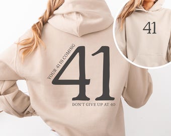 May include: Beige hoodie with a large black number 41 printed on the back. The text "Your 41 is coming" is printed diagonally across the number. Below the number, the text "Don't give up at 40" is printed.