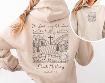 May include: A beige hoodie with a black and white graphic on the back. The graphic features a cross, hills, trees, and sheep. The text "The Lord is my Shepherd I lack Nothing Psalm 23:1-2" is printed below the graphic.