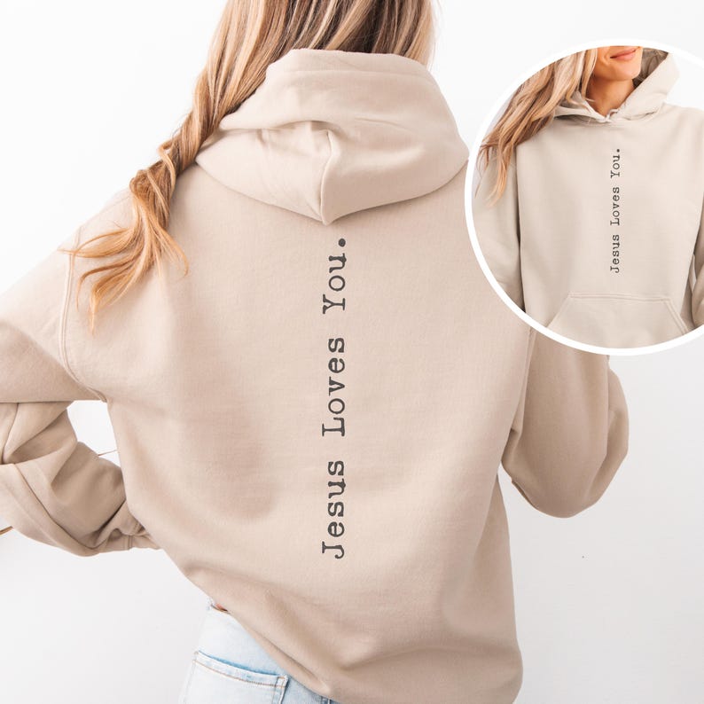 May include: A beige hoodie with the text "Jesus Loves You" printed vertically down the back. The hoodie has a drawstring hood and a front pocket. The image also shows a close-up of the hoodie with the same text.