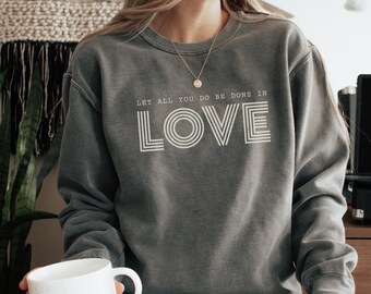 May include: A grey sweatshirt with the text "Let all you do be done in LOVE" in white lettering. The word "LOVE" is in a retro font with multiple lines.