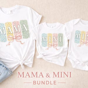 May include: White t-shirts and a babygrow with the words "MAMA" and "MINI" in pastel colours. The shirts have a floral design and a bow. The image also includes a pair of jeans, flowers, and white trainers.