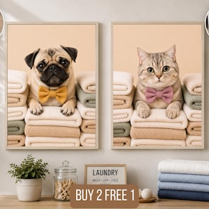 May include: Two framed wall art prints featuring a pug wearing a yellow bow tie and a tabby cat wearing a pink bow tie, both resting on stacks of folded towels. The prints are displayed above a laundry room counter with a glass jar and towels.