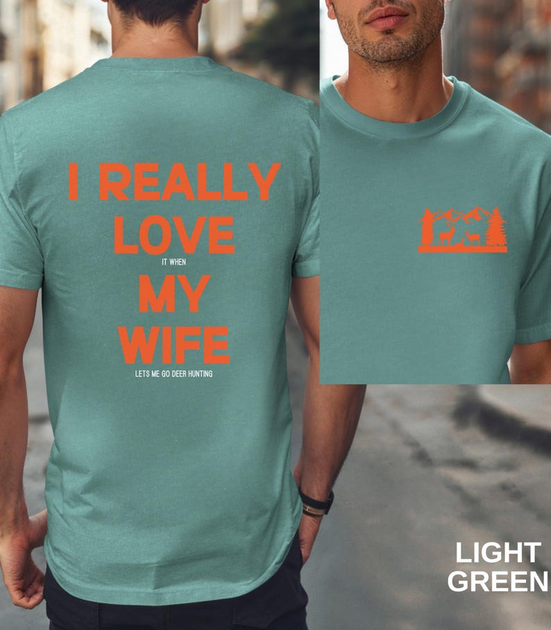 K&ouml;nnte beinhalten: Ein hellgr&uuml;nes T-Shirt mit dem Text "I really love my wife it when lets me go deer hunting" in Orange. Auf der R&uuml;ckseite des Shirts ist eine Silhouette eines Hirsches in einem Wald zu sehen.