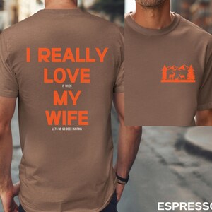 K&ouml;nnte beinhalten: Braunes T-Shirt mit dem Text "I really love my wife it when lets me go deer hunting" auf der R&uuml;ckseite und einer Silhouette eines Hirsches in einem Wald auf der Vorderseite.