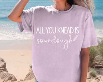 May include: A light purple t-shirt with the text "All you knead is sourdough" and a small wheat graphic.