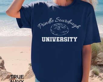 May include: A navy blue t-shirt with the text "Prindle Sourdough University" in white script and block letters, featuring a bread graphic. The words "True Navy" are printed at the bottom left.