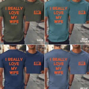 K&ouml;nnte beinhalten: Vier T-Shirts in verschiedenen Farben mit dem Text "I REALLY LOVE MY WIFE" und einer kleinen Grafik einer Bergszene mit einem Reh. Die Farben sind Salbei, Blautanne, Mitternachtsblau und Jeansblau.