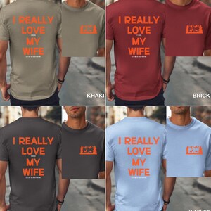 K&ouml;nnte beinhalten: Vier T-Shirts in verschiedenen Farben mit dem Text "I REALLY LOVE MY WIFE" und einer Grafik einer Bergkette mit einem Reh davor. Die Farben sind Khaki, Ziegel, Pfeffer und gewaschener Denim.