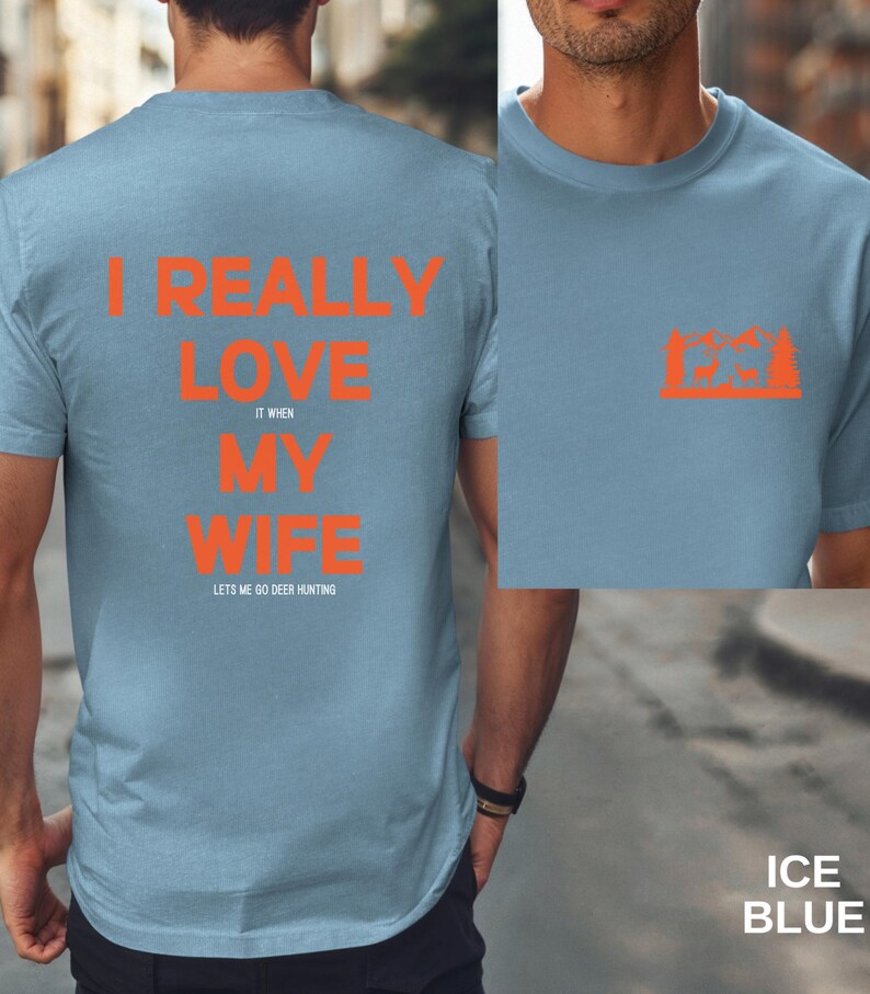 K&ouml;nnte beinhalten: Ein hellblaues T-Shirt mit dem Text "I really love my wife it when lets me go deer hunting" in orange gedruckt. Die R&uuml;ckseite des Shirts zeigt eine kleine orangefarbene Grafik eines Hirsches in einem Wald.