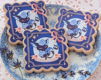 Puede incluir: Tres imanes cuadrados de madera con bordes festoneados que presentan una ilustración azul oscuro de un personaje con gorro de dormir sosteniendo una manta. El diseño incluye una cinta rosa, estrellas y el texto "NIGHT NIGHT" en una pancarta.