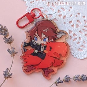 Puede incluir: Un charm de acrílico transparente con un personaje de dibujos animados montado en un pájaro rojo. El charm tiene un cierre rojo y un charm plateado en forma de ala. El fondo es una superficie rosa claro con ramitas de lavanda y un tapete de encaje blanco.