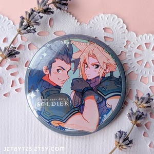 May include: A round button featuring two anime-style characters with the text "Honor your duty as SOLDIER!". The button has a blue and gray color scheme with the words "Shinra Crafted" at the top. The Etsy shop name "JETBYTES.ETSY.COM" is at the bottom.