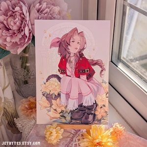 May include: An art print depicting a female character in a red jacket and pink dress, surrounded by yellow flowers. The illustration uses a soft, pastel colour palette and has a fantasy theme. The print is displayed near a window with natural light.