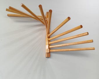 May include: A wooden wall-mounted towel rack with multiple arms extending out in a fan shape. The rack is made of natural wood and has a light brown finish.