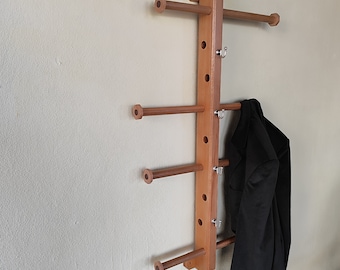 May include: A wooden wall-mounted coat rack with four horizontal rails and multiple hooks. The rack is made of light brown wood and has a natural finish. A black jacket is hanging on the bottom rail.