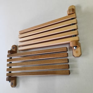 May include: Two wooden wall-mounted folding shelves with a light brown finish. The shelves are made of multiple slats that fold up and down. The shelves are mounted to the wall with metal screws.