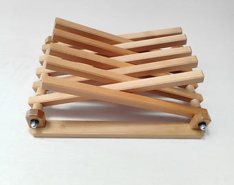 May include: A wooden laptop stand with a criss-cross design. The stand is made of light brown wood and has a natural finish. It is designed to elevate a laptop to a comfortable viewing angle.