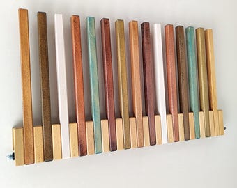 May include: A wooden wall-mounted coat rack with vertical wooden slats in various colours, including brown, white, and teal. The rack is mounted on a white wall and has a rectangular base.