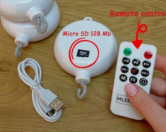 May include: White musical mobile with a hook for hanging, a remote control, and a USB charging cable. The mobile has a Micro SD card slot and says "Micro SD 128 Mb". The remote control has buttons for on, off, volume, and track selection.