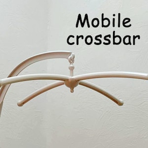 May include: White plastic mobile crossbar with four arms and rounded ends. The crossbar is designed to hold a baby mobile.