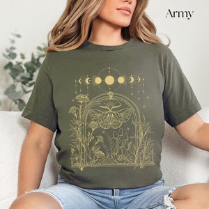 May include: A green t-shirt with a gold outline of a moth, flowers, mushrooms, and a crescent moon design. The text "Army" is in the top right corner of the image.