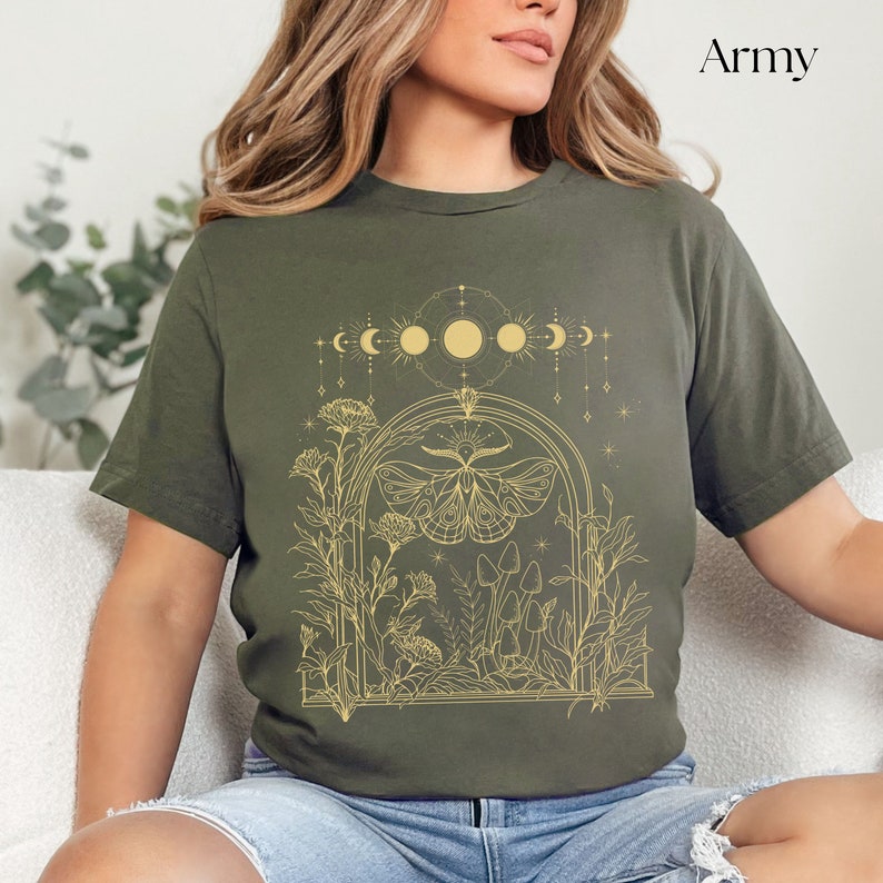 May include: A green t-shirt with a gold outline of a moth, flowers, mushrooms, and a crescent moon design. The text "Army" is in the top right corner of the image.