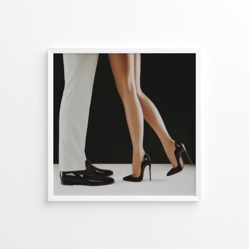 May include: A black and white photograph of a couple's legs and feet. The woman is wearing black high heels and the man is wearing black dress shoes. The background is black.