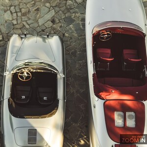 May include: A silver Porsche 911 and a silver speedboat are parked side-by-side on a stone driveway. Both vehicles have red interiors.