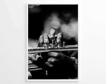 May include: A black and white photograph of a person's hand playing a trumpet. The hand is in focus, while the background is blurred.