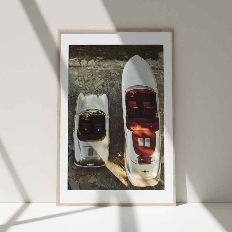 May include: A silver Porsche 356 Speedster and a silver speedboat are parked side-by-side on a cobbled driveway. Both vehicles are viewed from above.