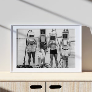 以下が含まれることがあります： 4人の人がダイビングヘルメットをかぶっている白黒写真。人々はビーチで一列に並んで立っています。ヘルメットはすべて異なるスタイルで、異なるデザインをしています。