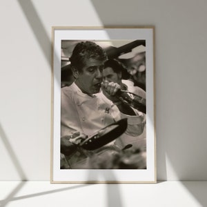 Peut inclure: Une photo en noir et blanc d'un chef portant une veste de chef blanche, tenant une po&ecirc;le et versant du vin dans un verre.