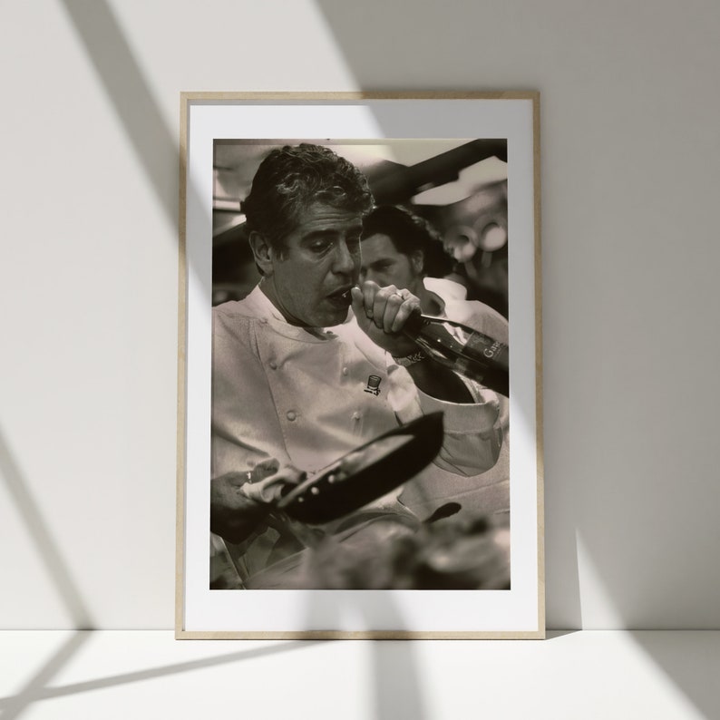 Peut inclure: Une photo en noir et blanc d'un chef portant une veste de chef blanche, tenant une po&ecirc;le et versant du vin dans un verre.