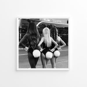 May include: Three people wearing black bunny costumes with white fluffy tails stand in a row facing away from the camera. They are in front of a black bus.