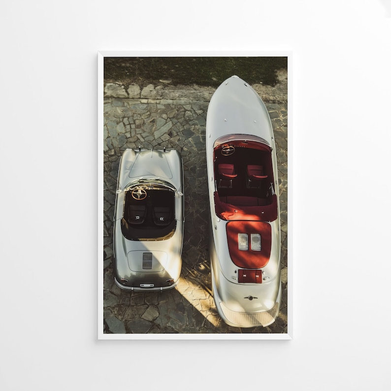 May include: A silver Porsche 356 Speedster and a silver speedboat are parked side-by-side on a stone driveway. Both vehicles have red interior details.