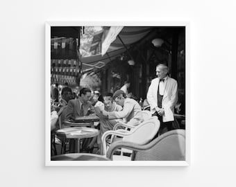 Könnte beinhalten: Schwarzweißfoto von vier Männern, die an einem Cafétisch sitzen. Drei Männer schauen auf ein Dokument, während ein Kellner hinter ihnen steht. Das Café ist im Freien mit einem gestreiften Vordach über ihnen.