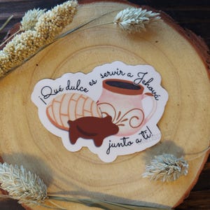 Peut inclure: Un autocollant avec une tasse rose, une p&acirc;tisserie concha et une p&acirc;tisserie en forme de cochon marron. Le texte "&iexcl;Qu&eacute; dulce es servir a Jehov&aacute; junto a ti!" est en script noir. L'autocollant est sur une surface en bois.