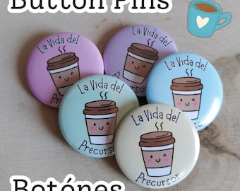 May include: A collection of round button pins in pastel colors, each featuring a cartoon coffee cup design with the text "La Vida del Precursor." The words "Button Pins" and "Botónes" are also visible.