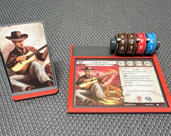 May include: A red and black game board with a card titled "Ashcan Pete" featuring a man playing a guitar. The board has a counter with four dials, each with numbers 0-5. The card text reads "Drifter: You begin the game with Duke in play. Discard a card from your hand: Ready an asset you control. (Limit once per round.)  In effect: +2 Ready Duke. "C'mon, boy, we got work to do."