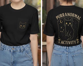 May include: Black t-shirt with a gold cat design on the pocket and back. The back of the shirt features the text "PURRANORMAL ACTIVITY" with a cat illustration, a moon, and a haunted house.