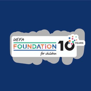 Peut inclure: Logo de la Fondation UEFA pour les enfants sur fond bleu. Le logo présente les mots "UEFA FOUNDATION for children" en différentes couleurs, avec un grand "10" et le mot "YEARS". Une forme de nuage entoure le logo.