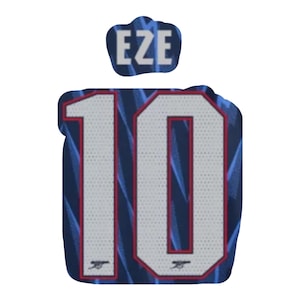 Pode incluir: Uma camisa azul marinho e branca com o número 10 em branco com contorno vermelho. O nome "EZE" está acima do número. A camisa tem um padrão azul e um logotipo da equipe na parte inferior.