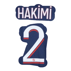 Puede incluir: Un parche azul marino con el nombre "HAKIMI" en letras blancas sobre el número "2". El número es blanco con un contorno rojo, sobre un fondo azul marino. El parche tiene un aspecto texturizado.