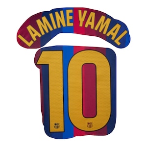 Può includere: Il retro di una maglia sportiva con strisce verticali blu e rosse, il nome LAMINE YAMAL stampato in testo giallo arcuato sopra il grande numero 10 giallo, che presenta piccoli stemmi della squadra alla base di ogni cifra.