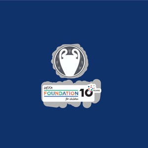 May include: A blue background with the UEFA Foundation logo. The logo includes a white and gray emblem of a trophy, and text that reads "UEFA FOUNDATION for children" with the number "10 YEARS".