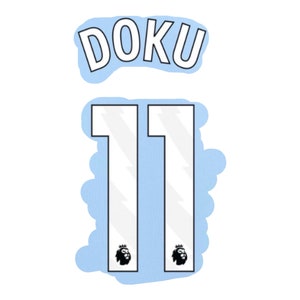 Può includere: Una maglia da calcio blu chiaro con il nome "DOKU" e il numero "11" sul retro. La maglia ha un contorno bianco e un piccolo stemma di leone nero.