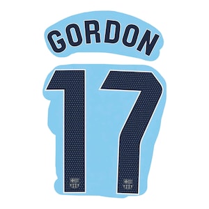 Pode incluir: Um gráfico de camisola desportiva azul claro com o nome GORDON em letras azul-marinho escuro arqueadas sobre o número 17. O número 17 é azul-marinho escuro com um padrão de pontos brancos e inclui um pequeno emblema do FC Barcelona na base.