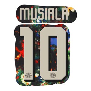 May include: A sports jersey name and number decal featuring the name MUSIALA in beige block letters above the number 10. The design has a dark, multicoloured abstract pattern background with small circular team logos at the base of each digit.